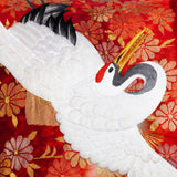 Detail of red silk Japanese Crane cushion showing white crane with bent neck and open wings over a red and gold woven floral background.