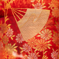 Gold fan on red silk pillow, detail of red textile with woven gold flowers.