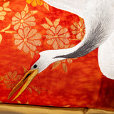 Detail of kimono cushion textile showing head and neck of white silk embroidered crane with gold beak. Red and gold floral woven background.